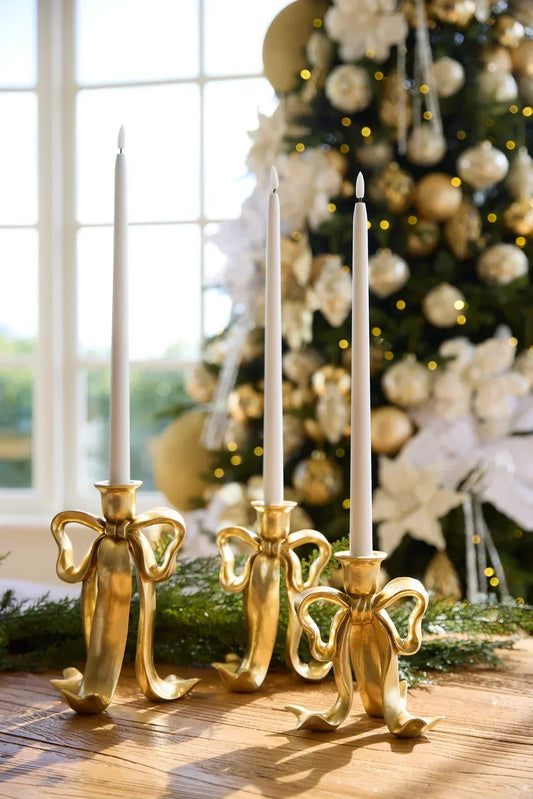 Gold bow candle holders with white tapers, festive Christmas tree backdrop, elegant holiday home décor