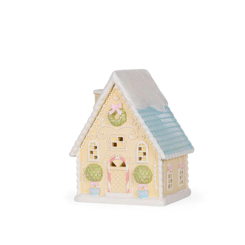 Pastel gingerbread house with wreaths, bows, and snowy roof — festive holiday décor
