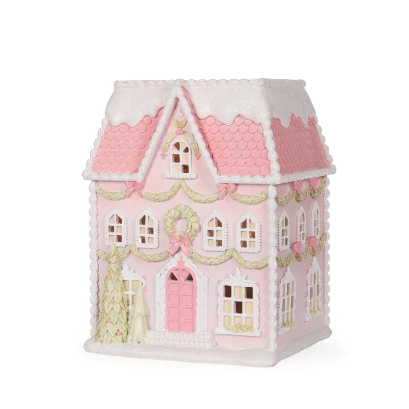 Pink gingerbread-style house with white trim, festive wreaths, and snowy roof for holiday décor
