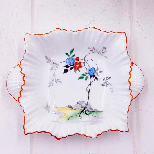 Hand-painted ceramic plate with floral design, scalloped edges, and orange trim for vintage home decor