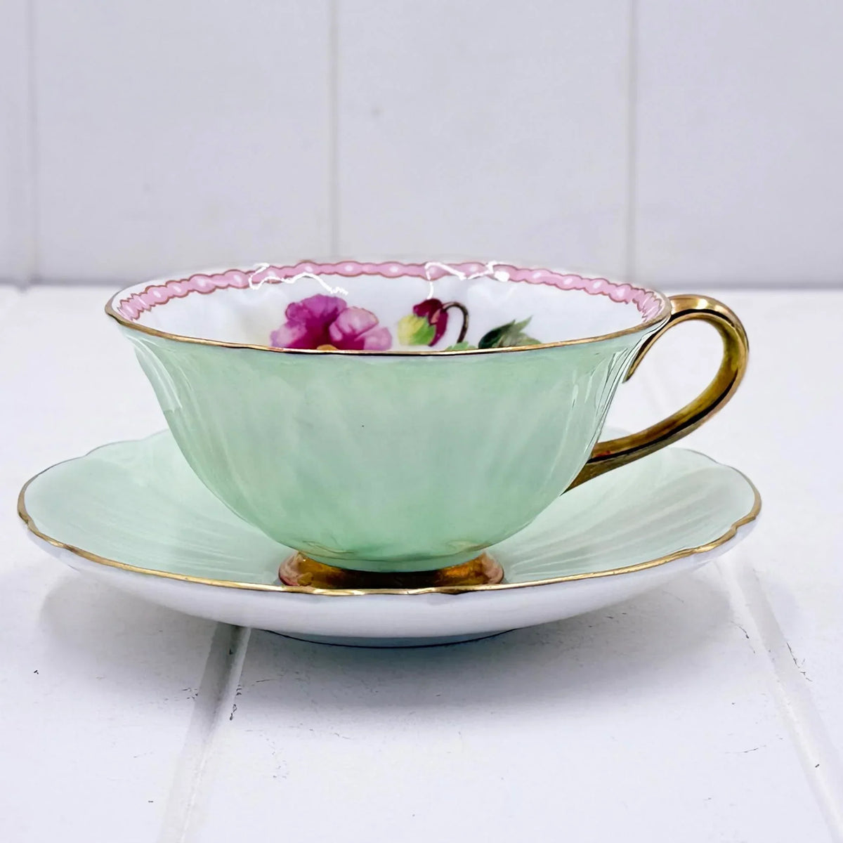 Mint green vintage teacup with pink floral interior, gold trim, and matching saucer for elegant home décor