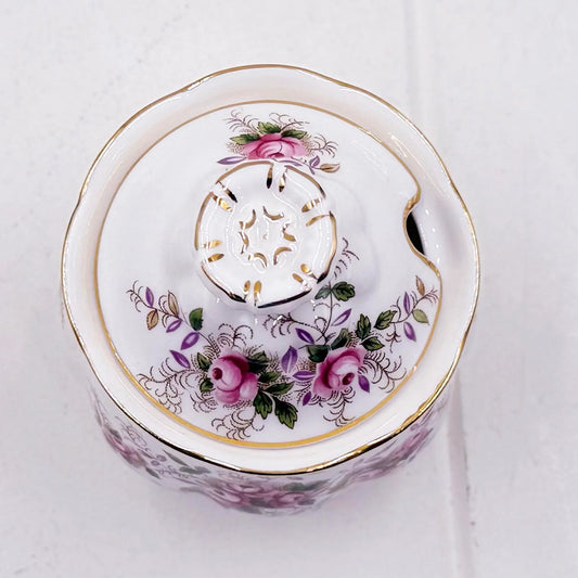 A white Royal Albert Lavender Rose preserve/sugar/jam pot with a floral design featuring pink roses, green leaves, and gold accents, photographed from a top-down angle on a light textured background.