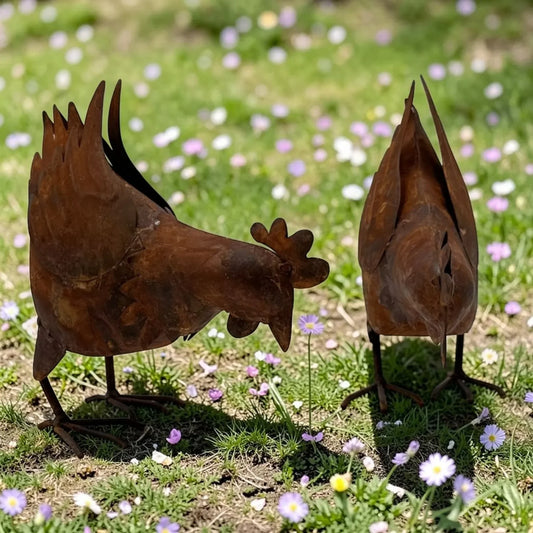 Rustic metal rooster and hen garden statues on grass with wildflowers, outdoor home decor