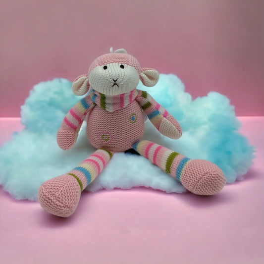 Knitted pink monkey toy with rainbow stripes, sitting on fluffy cloud against pink background