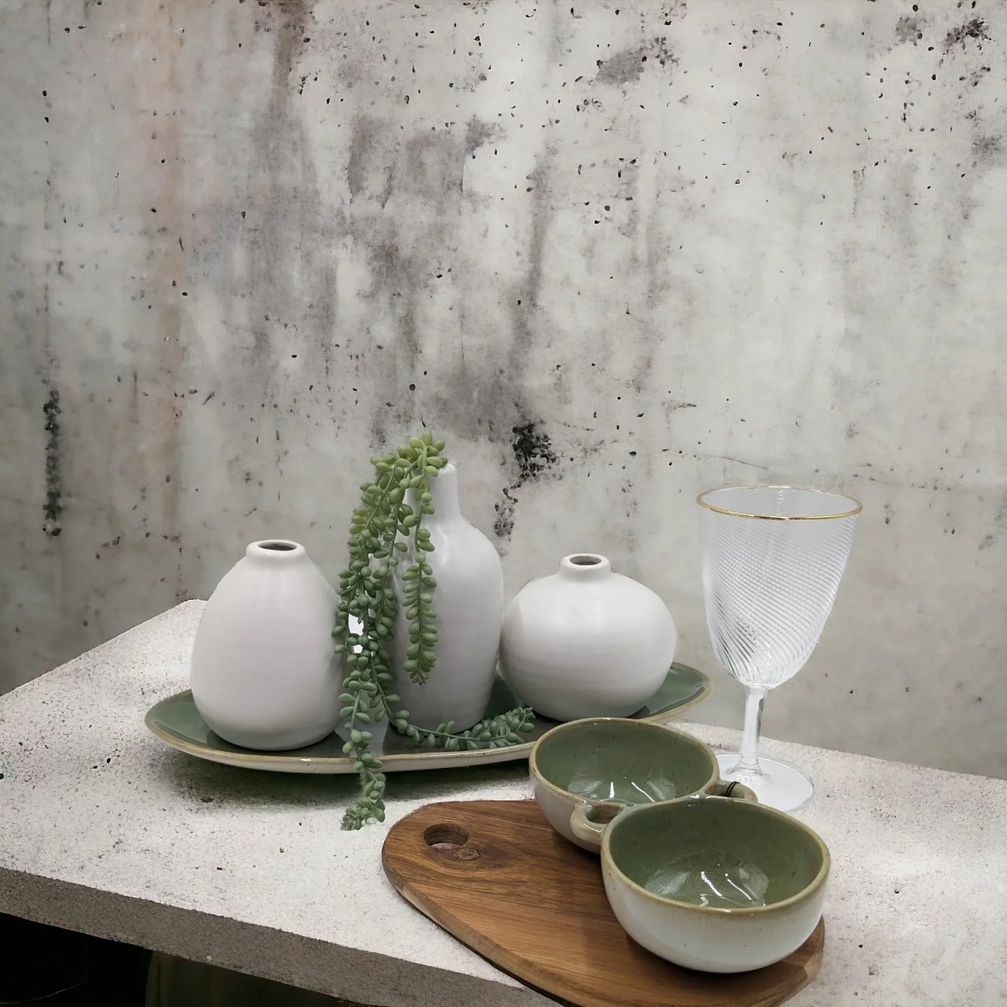 Minimalist white ceramic vases, green bowls, and textured glassware on concrete surface for modern home décor