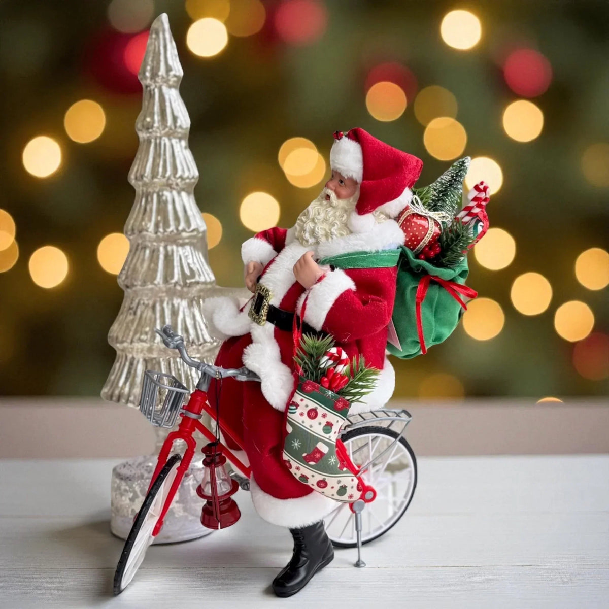Santa Claus figurine on red bicycle with Christmas tree and gifts, festive holiday decor