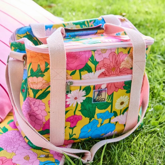 Vibrant floral cooler bag with pink straps, perfect for picnics and outdoor gatherings on grass.