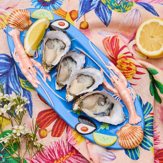 Blue seafood platter with oysters, shrimp, lemon, and shells on floral tablecloth
