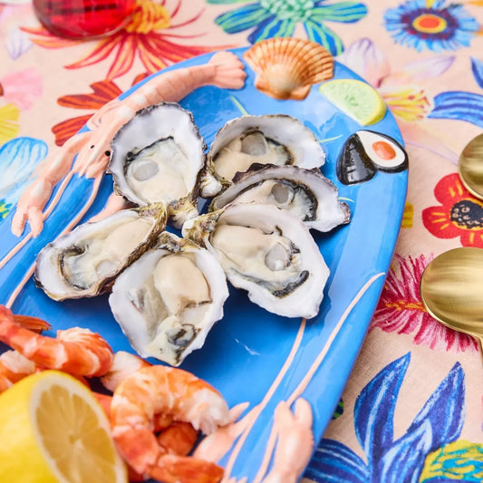 Blue seafood platter with oysters, shrimp, lemon, and shell decor on floral tablecloth
