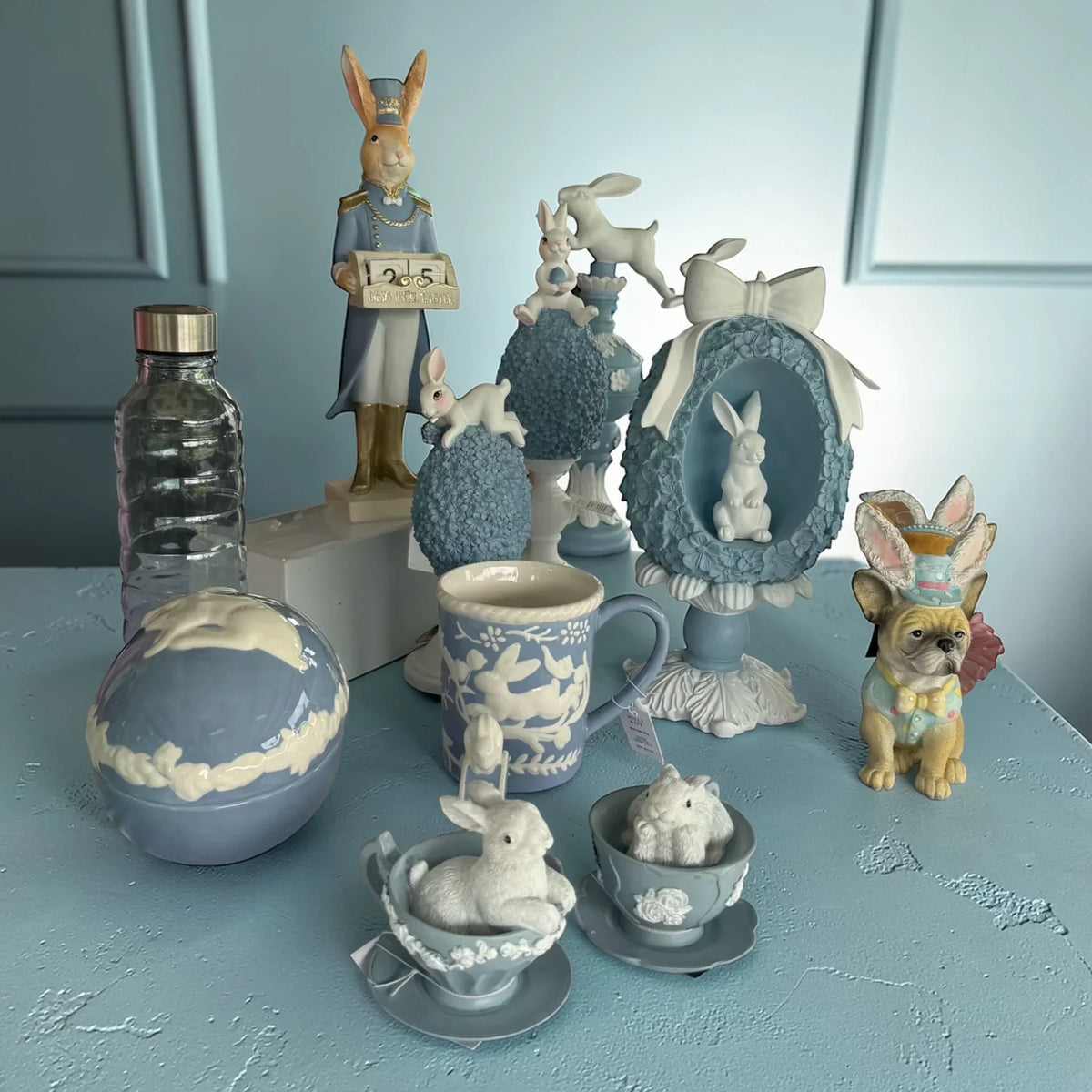Easter bunny figurines, blue ceramic decor, and vintage-style home accessories on a pastel table