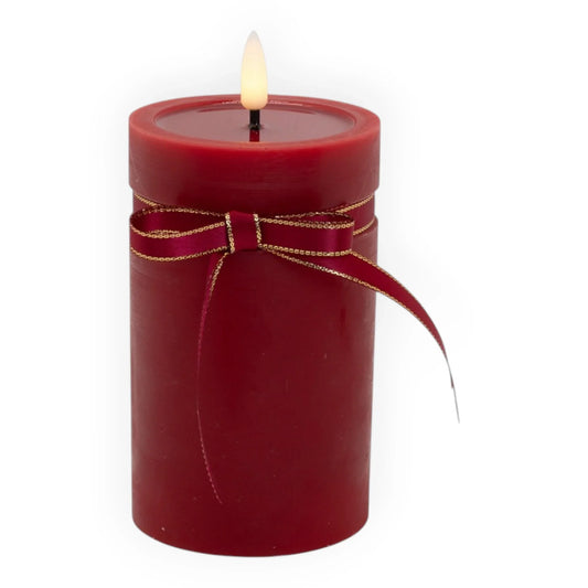 Red pillar candle with gold-trimmed ribbon bow, glowing flame for home décor ambiance
