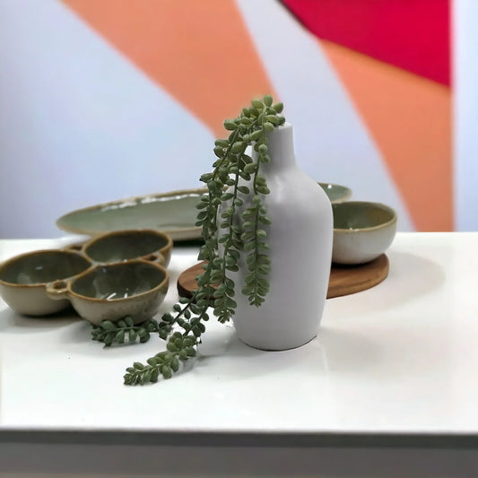 White ceramic vase with trailing succulent, green ceramic bowls, and wooden coasters on white shelf