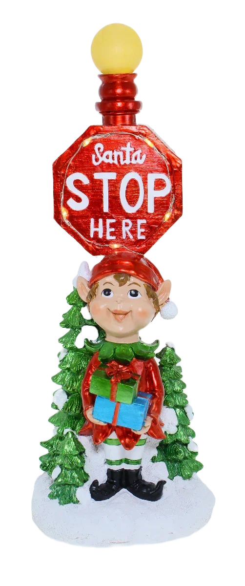 Festive elf holding gifts under Santa Stop Here sign, holiday décor with green trees and snow