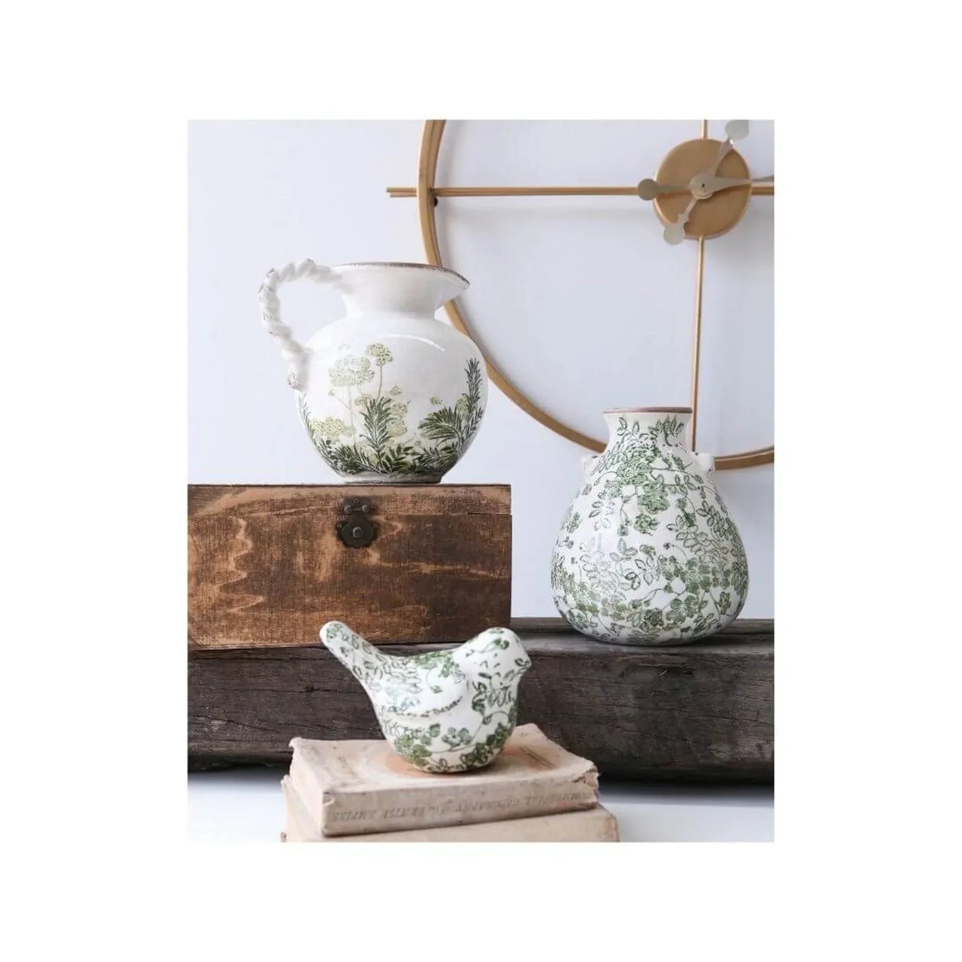 White ceramic pitcher, vase, and bird figurine with green botanical print, styled on rustic wood and books for home décor.
