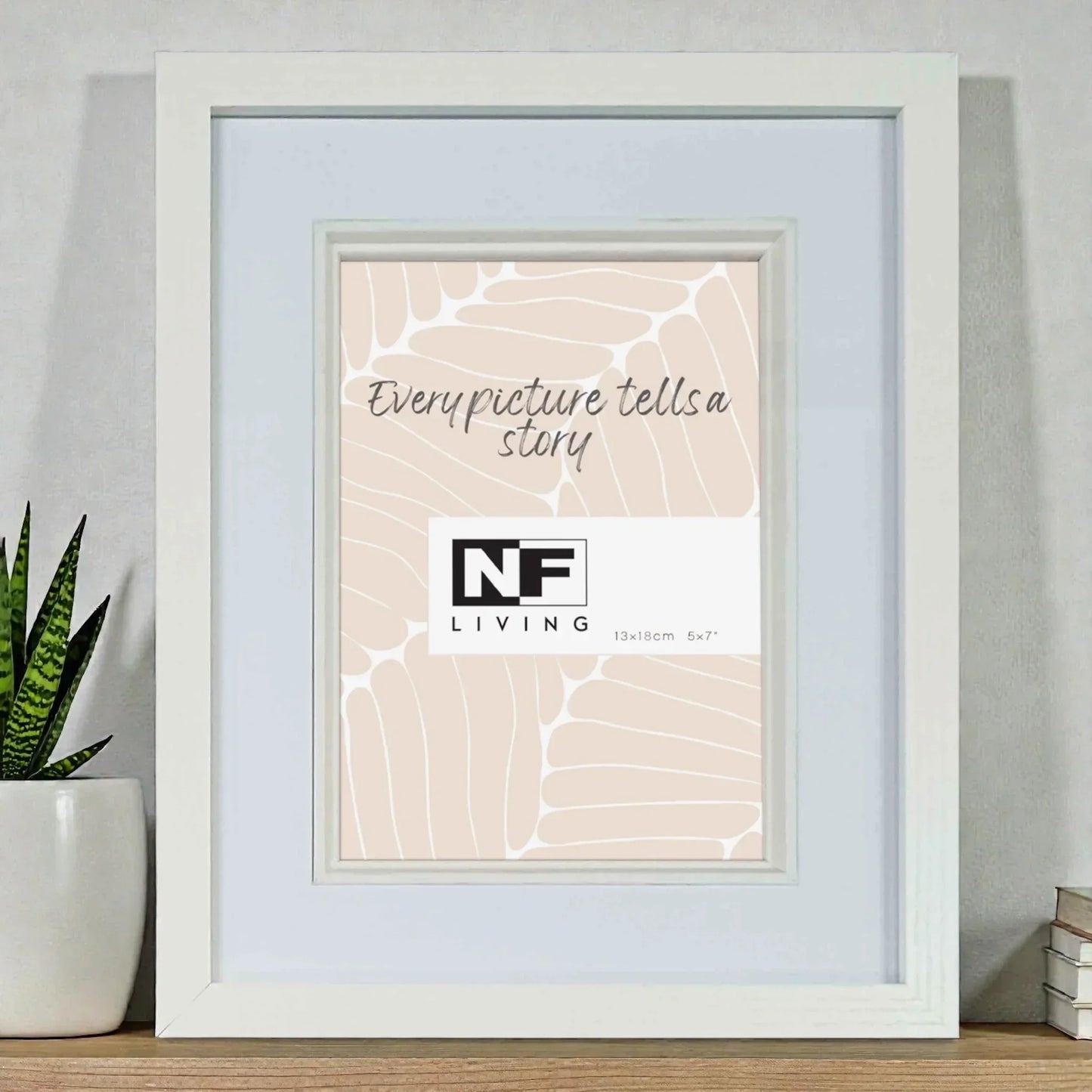 White picture frame with blush abstract print, 'Every picture tells a story' text, beside succulent plant